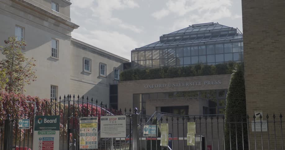 A university building behind an iron gate with several signs hanging