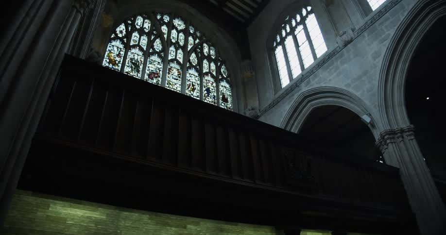 Sun shines through arched stained glass window into interior of a cathedral