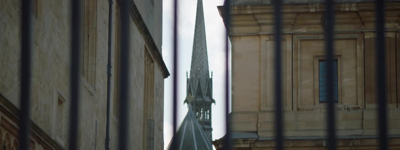 A view of a church steeple through a wrought iron fence with pointed pickets