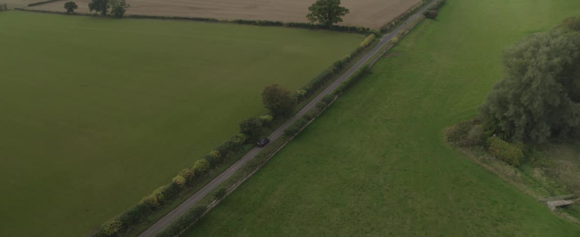 Aerial scene of a narrow street with a stopped vehicle and natural and agricultural corners next to it