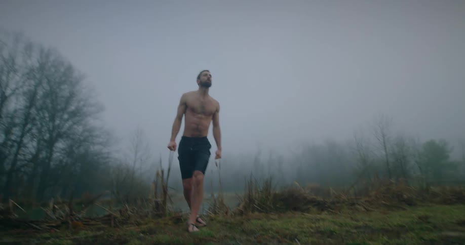 A shirtless man standing up on the shore of a foggy lake