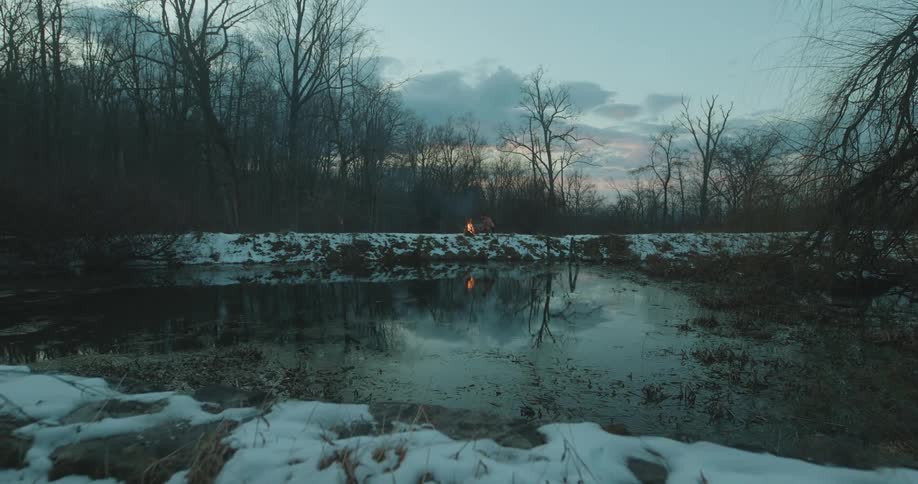 A campfire at the other side of a frozen lake at sunset