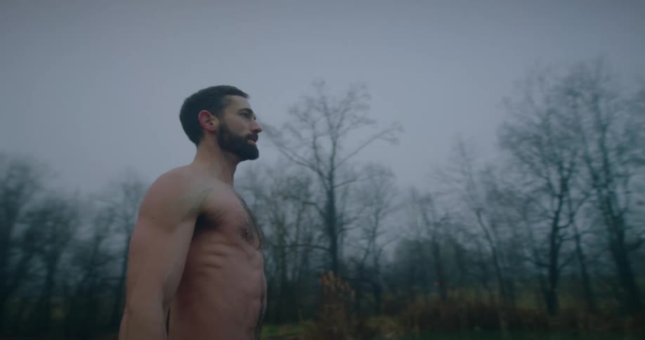 Man without a tshirt and just shorts with a concentrated facial expression in front of a greenish lake on a foggy day