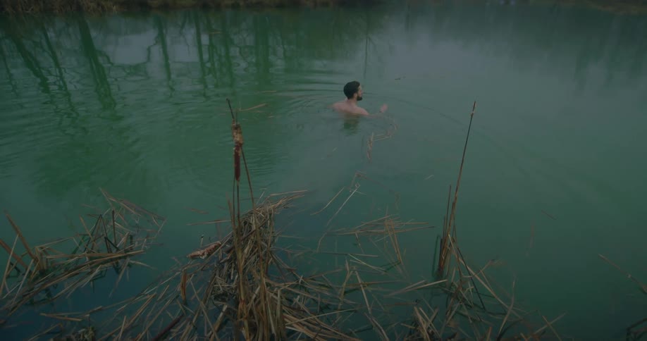 Man in shorts enters a greenish lake