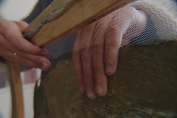 A hand separates green handmade paper from a wire screen
