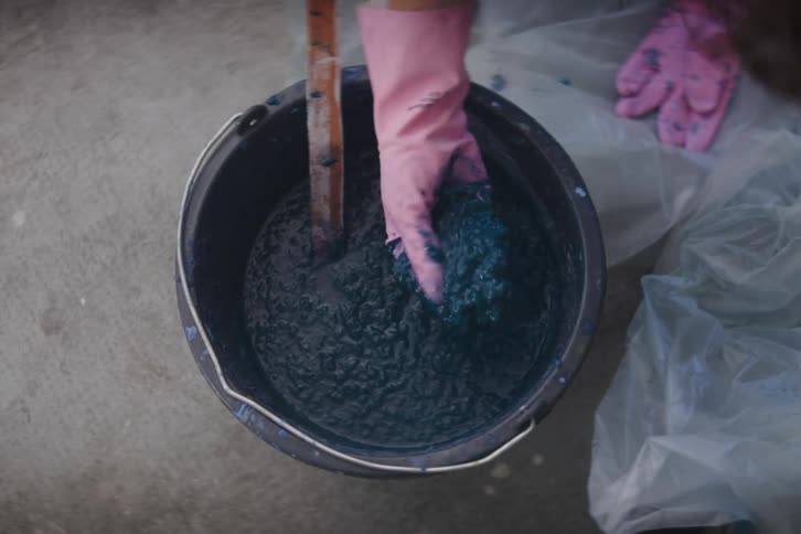 Woman hand with a glove being placed inside a bucket of sticky liquid