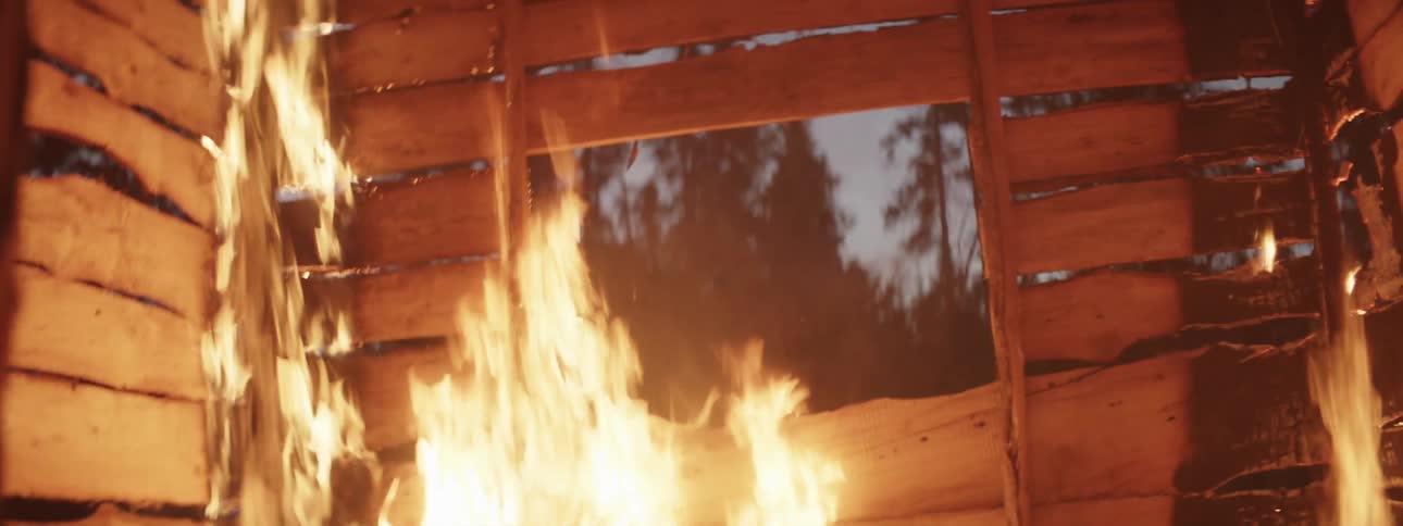 Small wooden cabin on fire in the middle of the forest