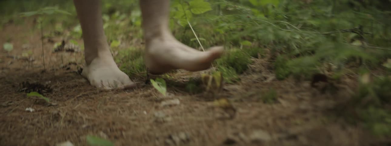 Legs of a barefoot person walking along the ground in nature