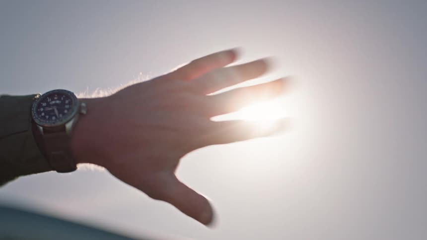 Point of view of a mans hand pointing to the sky with solar reflection and wearing a watch on his wrist