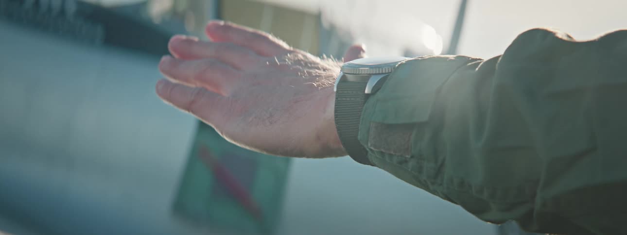 Hand of a man with a clock raised towards the sun