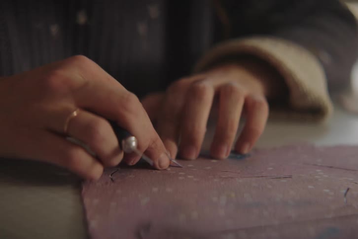 A persons hand using a cutting tool to cut a fillet from a lilac object