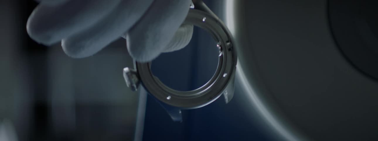 Closeup of a persons hand with a glove holding a round metal object that is being shaped in a moving machine