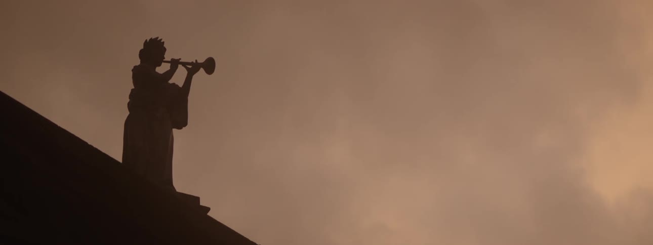 Monument of a woman playing an instrument on the roof of a building overlooking a reddish cloudy sky