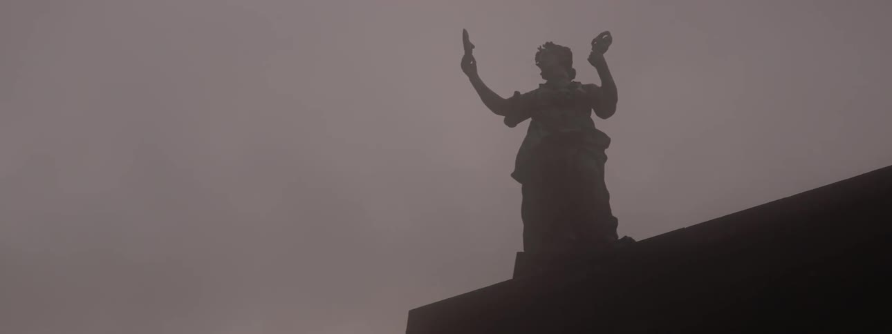 Silhouette of a statue on the roof of a building under an overcast sky