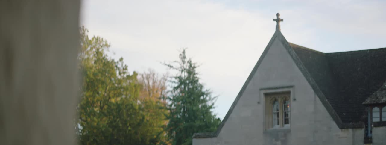 A white house with a black cross on top surrounded by trees