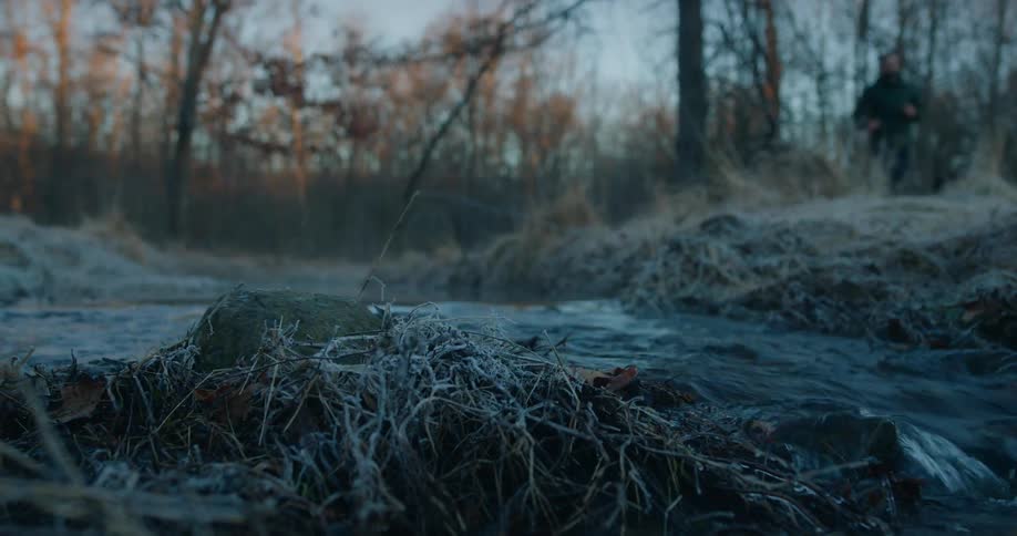 Running water in a river in a winter forest with a man running in the background