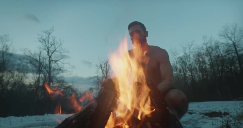 Man putting firewood on his bonfire in the middle of the snowy forest