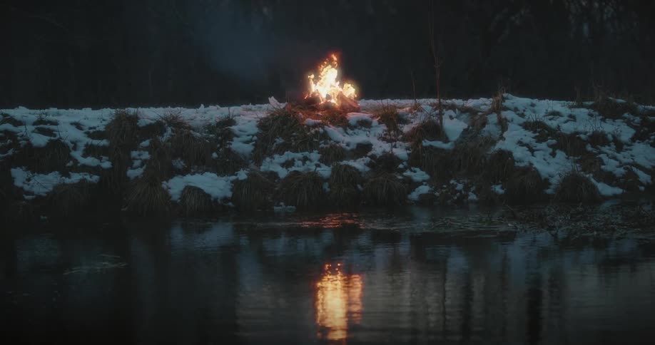A fire burns on a riverbank