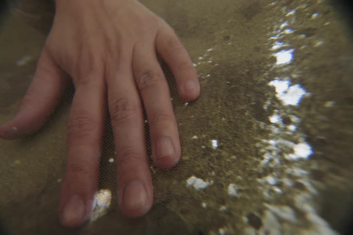 A woman rubs her hand across a green handmade paper behind a wire screen