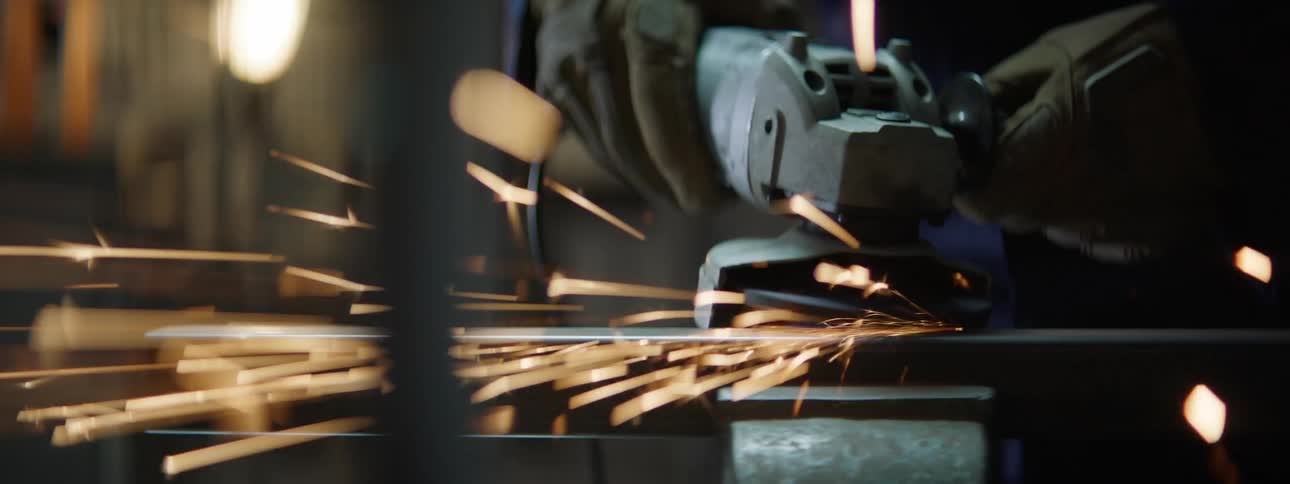 As a metalworker sands a metal bar sparks fly off it