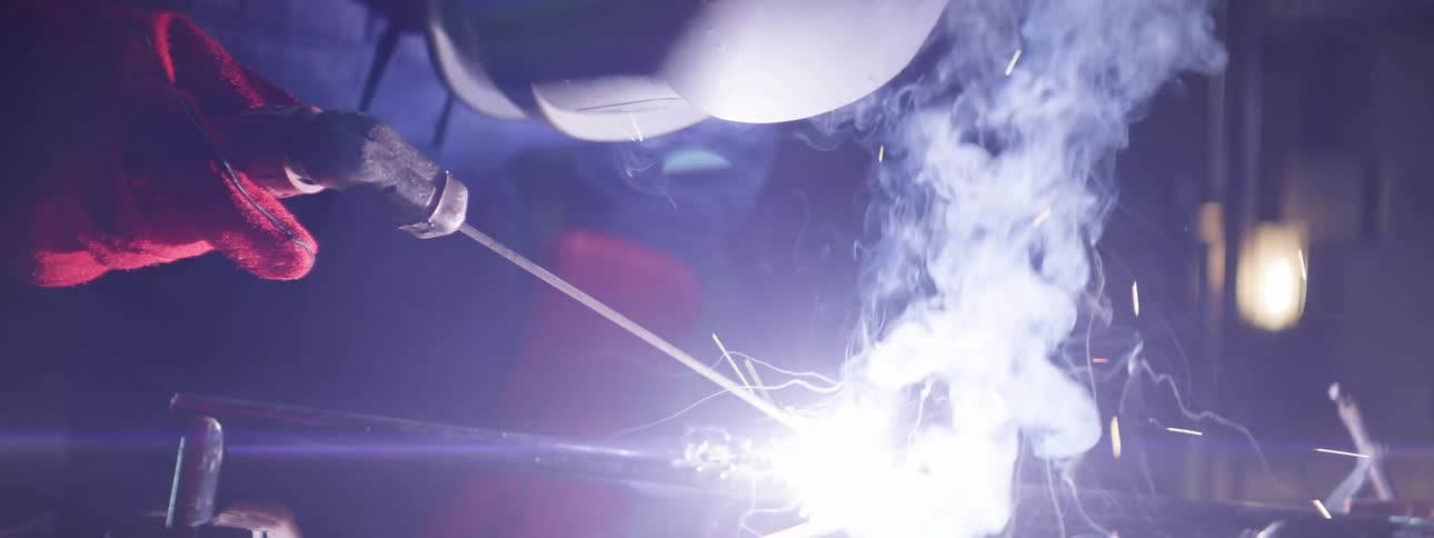 A man is welding a piece of metal in a dark workshop