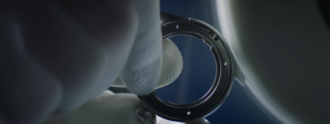 Extreme closeup of a persons hand with protective gloves holding a small cylindrical abstract object that is being shaped by a manufacturing machine