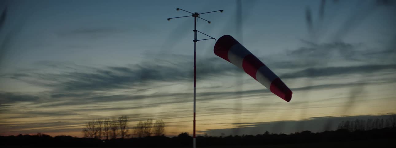 Windsock in an outdoor environment with the silhouette of forests and mountains on the horizon on a reddish cell morning