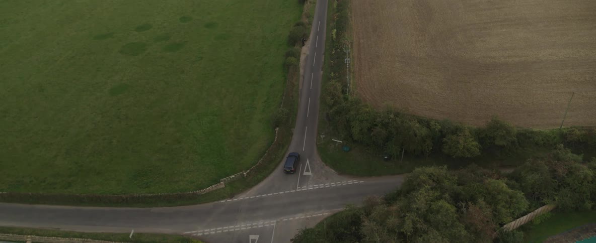 Aerial panorama of a black vehicle traveling on a road with natural and agricultural fields around it