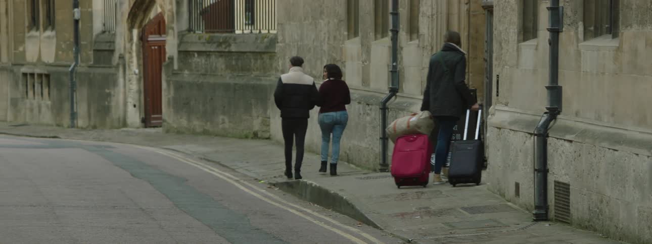 Woman walking on the sidewalk carrying suitcases and turning into an establishment