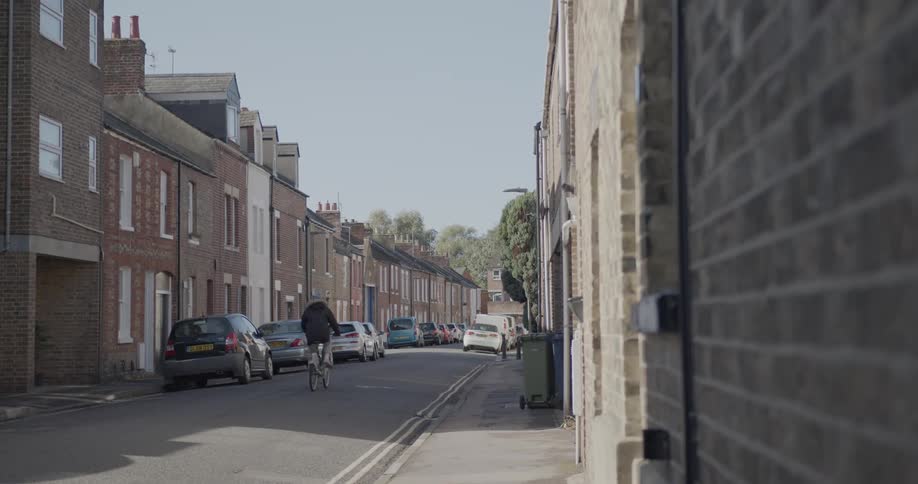 Street of a suburban city with parked vehicles and a person passing by on a bicycle