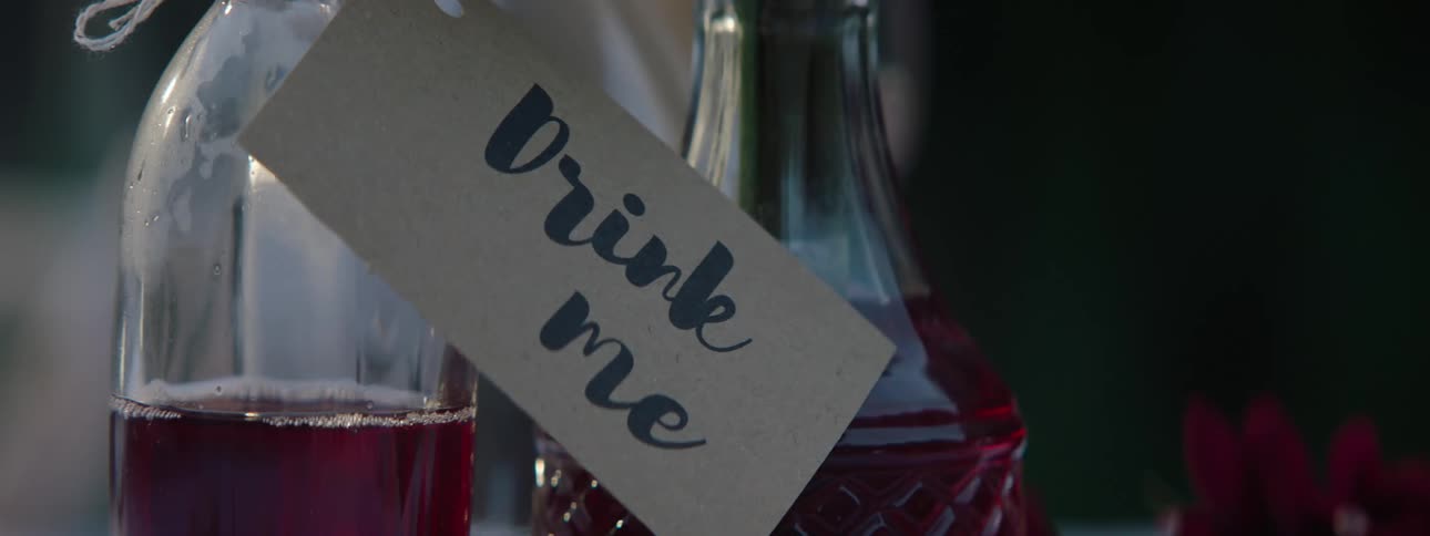 Two jugs with red liquid and a sign saying drink me