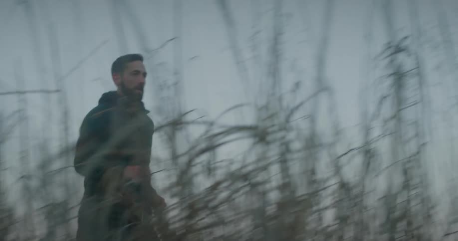 A man jogs outdoors in an area with tall grassy weeds