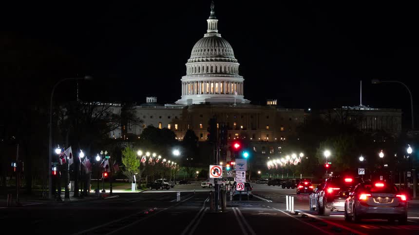 A white domeshaped building and in front there is car traffic on a street at night