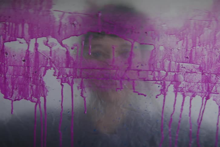 A woman looks through glass covered in purple paint