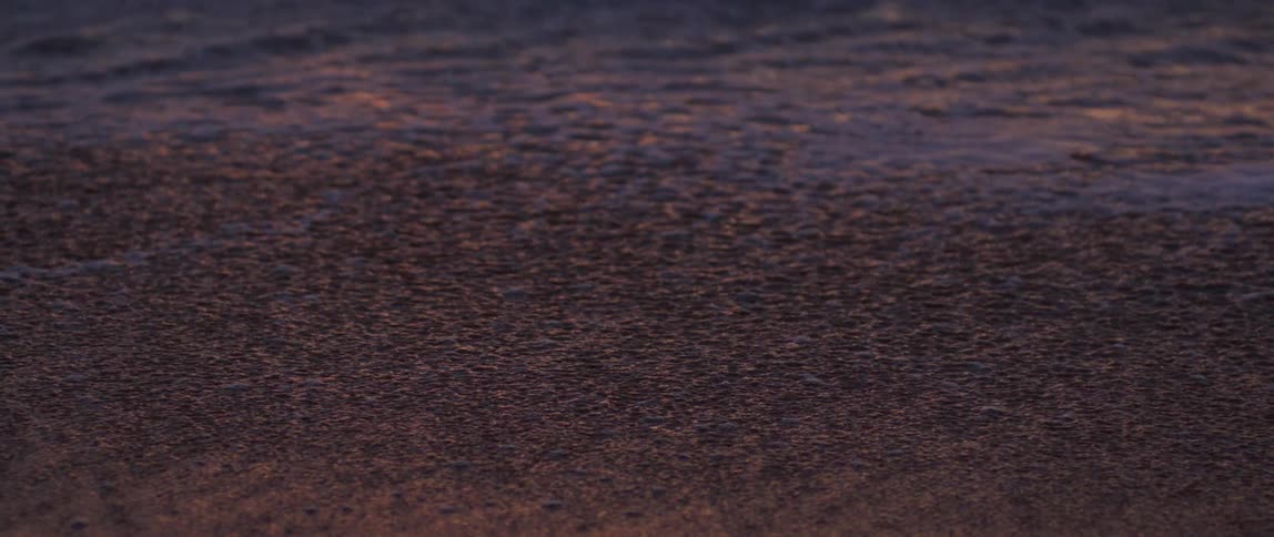 Sea water returning and the beach sand appearing with the morning sun reflection