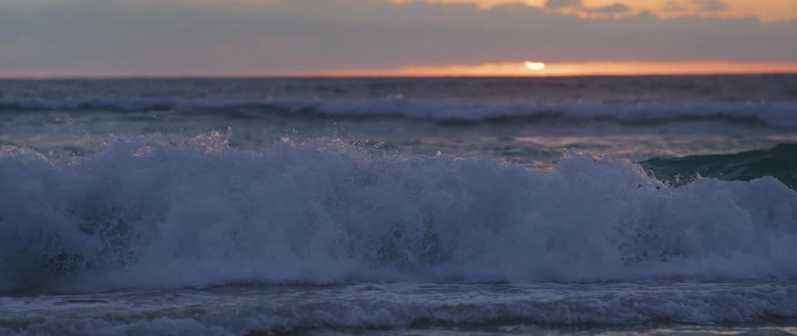Slow motion footage of ocean waves crashing into the beach at sunrise