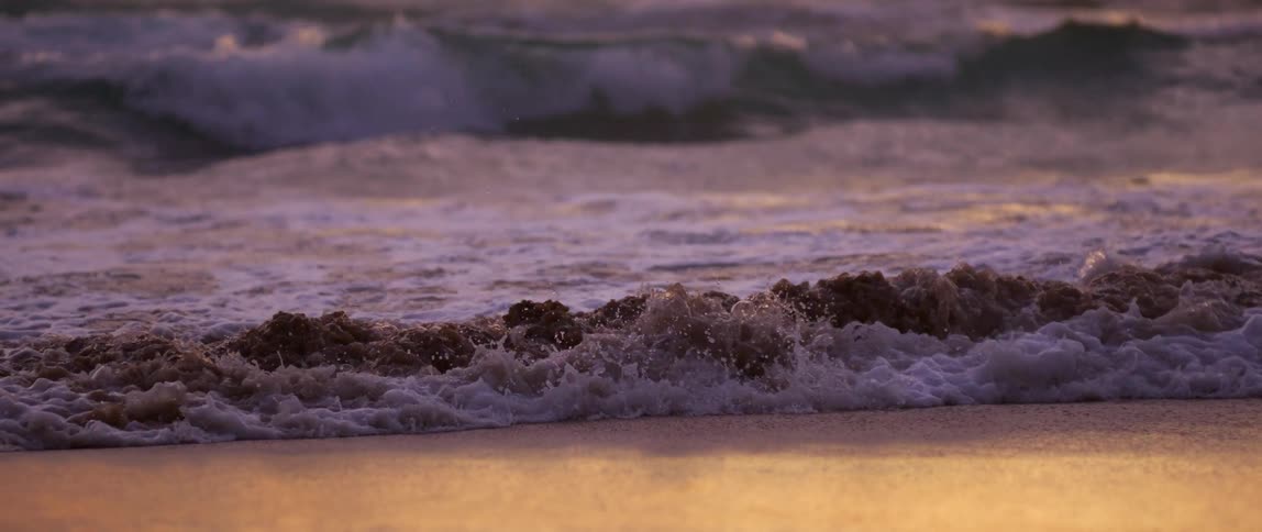 Waves on the edge of the beach with the reflection of the sun at dawn