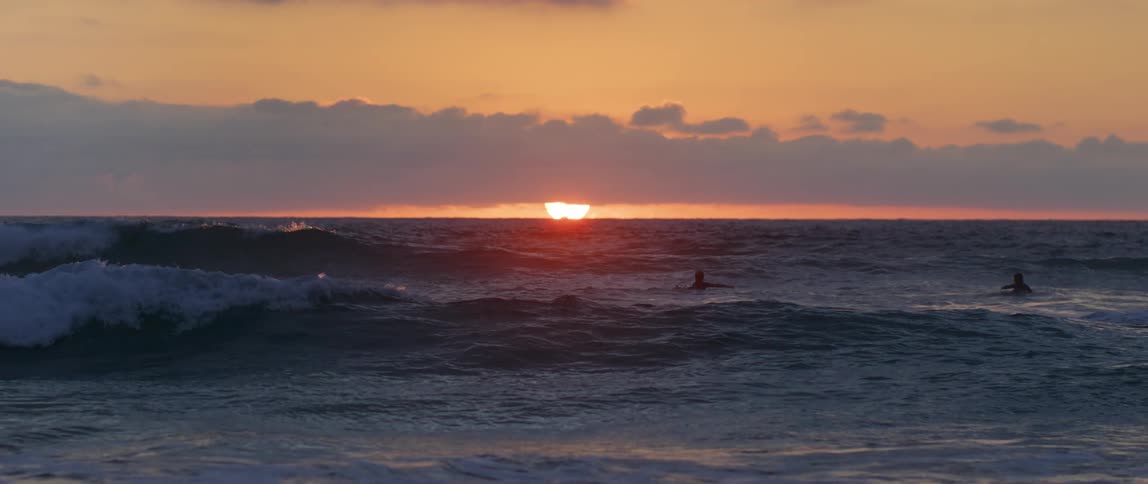 Landscape of a beach with two people inside and the reddish sunset on the horizon