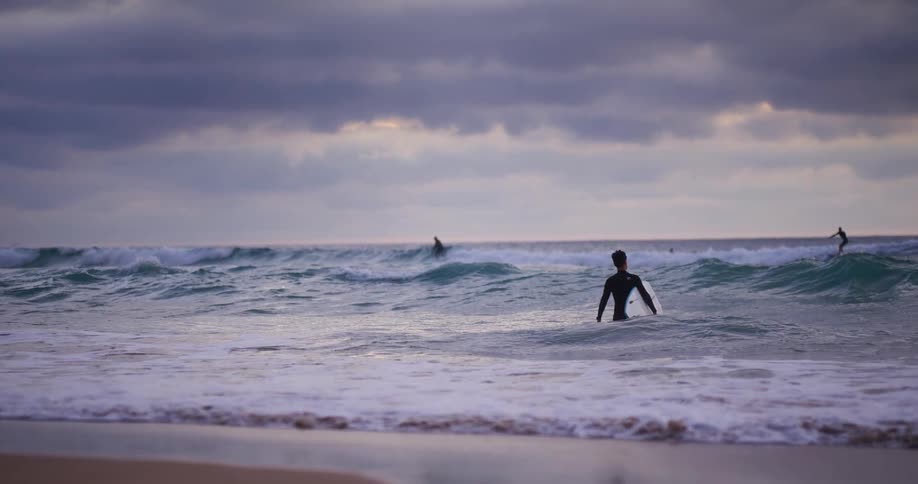 Surfers ride the waves while one surfer walks toward the others