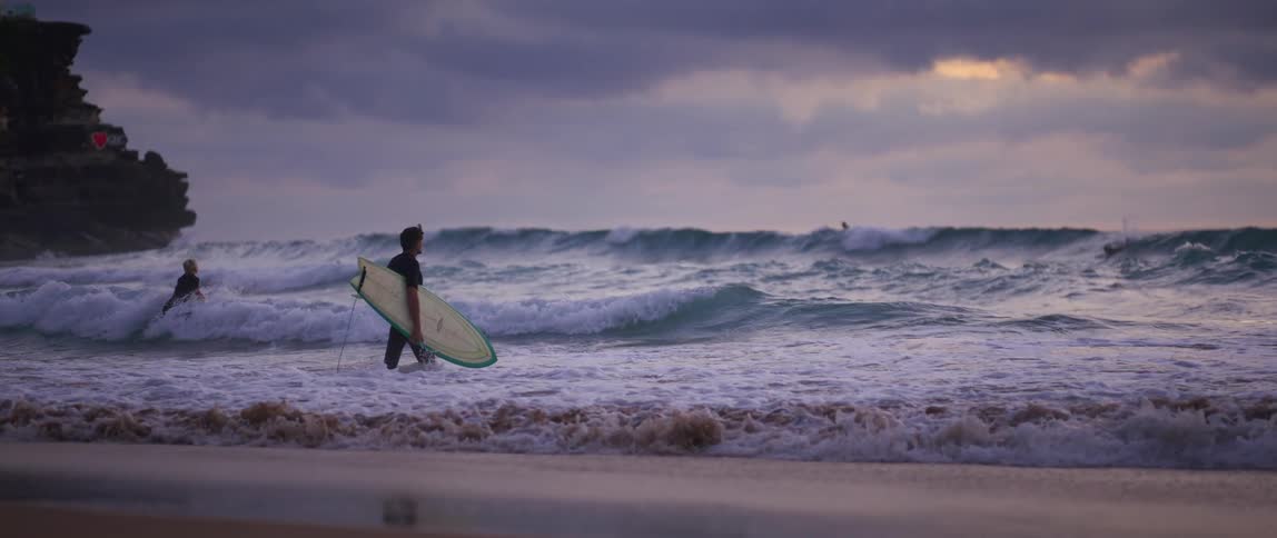 Surfers carry surfboards into foaming surf on an overcast day