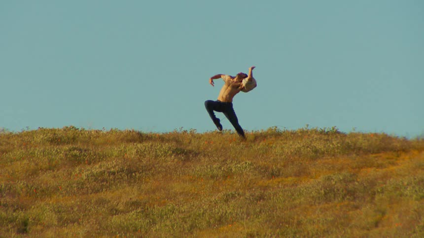 A man dances in slow motion on a hillside on a sunny summer day
