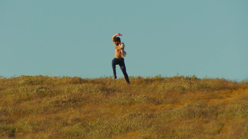 A young man dances on a grassy plain