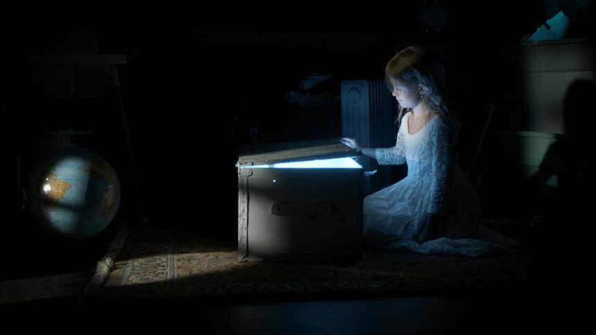 Girl in a dark room opening a box shining with a bright light
