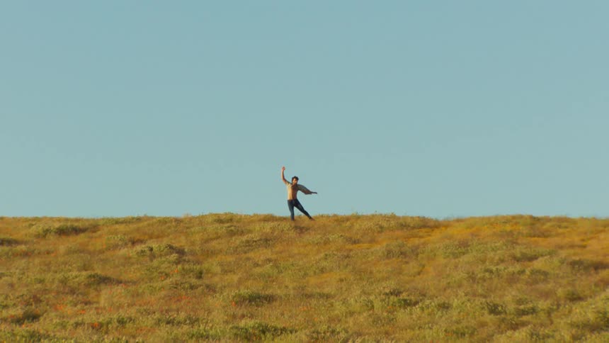 Man dancing scenically on a grassy hill