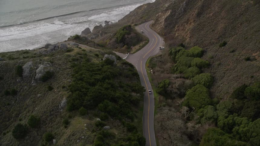 A car drives on a road that leads to a coast