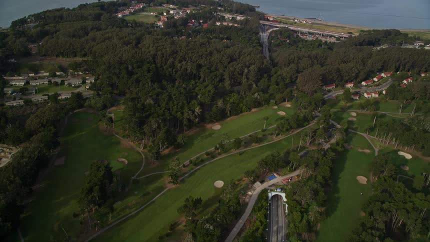 Traffic drives by a golf course and through a tunnel toward a bridge to the city