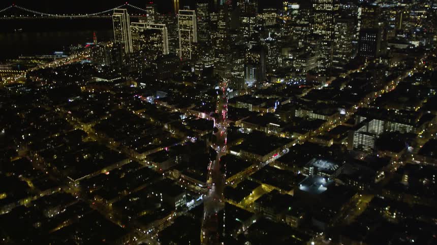 A city at night with several street lights and residences on and in the background there is a city center with several tall buildings