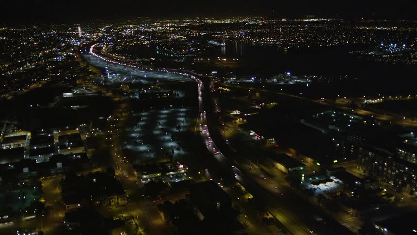 Aerial panorama of an extensive highway with vehicle traffic at night and surrounding a metropolis with urban and residential buildings