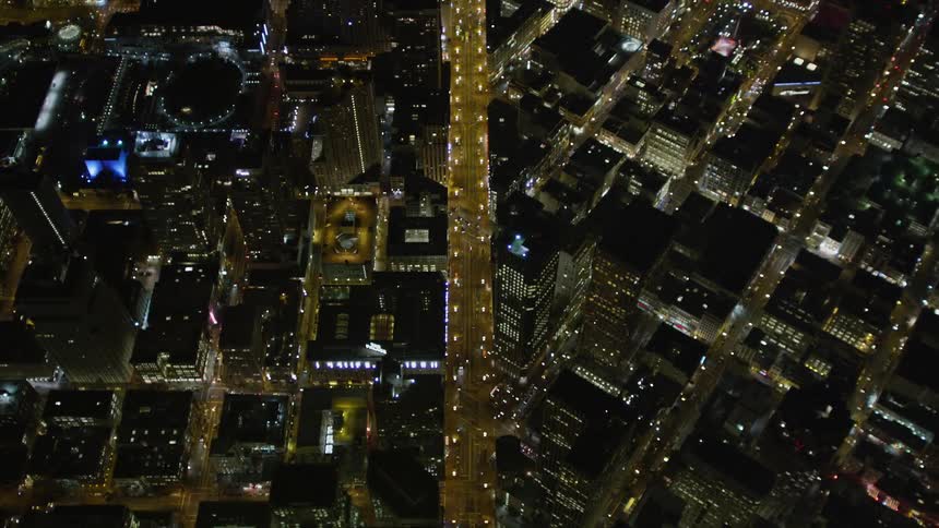 An aerial view of a street with several cars passing by in a city at night