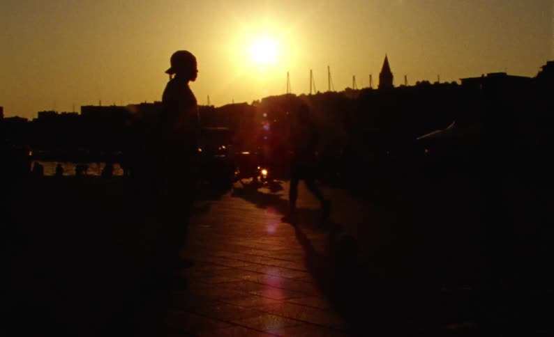 Street in a city on the edge of a lake with the silhouette of people walking and playing ball and the reflection of the sun in the late afternoon